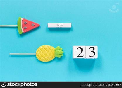 Wooden cubes calendar date June 23rd and summer fruits candy pineapple, watermelon lollipops on stick on blue background. Concept vacation or holidays Creative Top view Flat lay Template.. Wooden cubes calendar date June 23rd and summer fruits candy pineapple, watermelon lollipops on stick on blue background. Concept vacation or holidays Creative Top view Flat lay Template