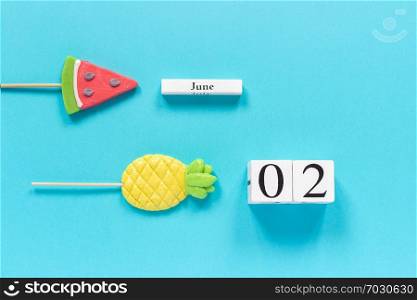 Wooden cubes calendar date June 2nd and summer fruits candy pineapple, watermelon lollipops on stick on blue background. Concept vacation or holidays Creative Top view Flat lay Template.. Wooden cubes calendar date June 2nd and summer fruits candy pineapple, watermelon lollipops on stick on blue background. Concept vacation or holidays Creative Top view Flat lay Template