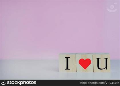 Wooden cubes with i love u symbol heart on the pink background and copy space.
