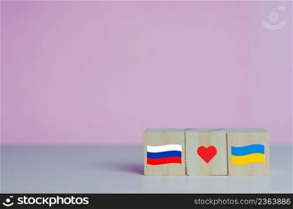 Wooden cubes with russia flag symbol and ukraine flag with red heart icon on background.