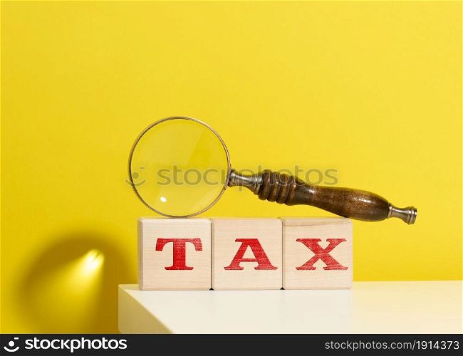 wooden cubes with the inscription tax and a brown magnifying glass on a yellow background