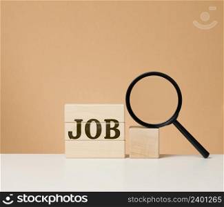 Wooden cubes with the inscription work and a black magnifier on a white table. Job search, unemployment