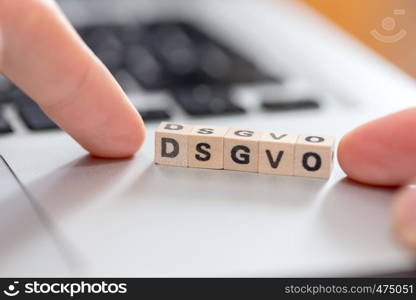 Wooden cubes with the letters ?DGSVO? for Datenschutzgrundverordnung are lying on a laptop
