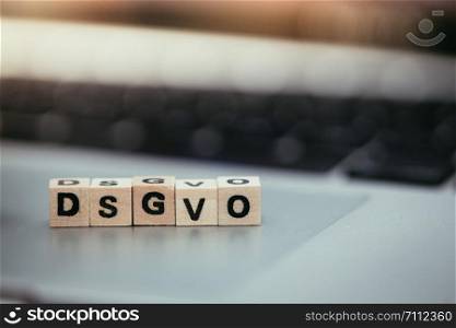 Wooden cubes with the letters ?DGSVO? for Datenschutzgrundverordnung are lying on a laptop