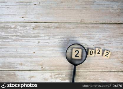 wooden cubes with the text 2022 with magnifying glass on wooden background top view, copy space modern design, New Year concept space for text. wooden cubes with the text 2022 with magnifying glass on wooden background top view, copy space modern design, New Year concept