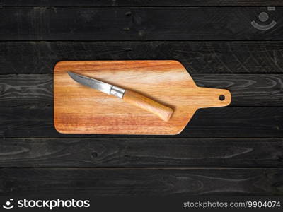 Wooden cutting board and pocket knife on black wood table background. Wooden cutting board and pocket knife on black wood table