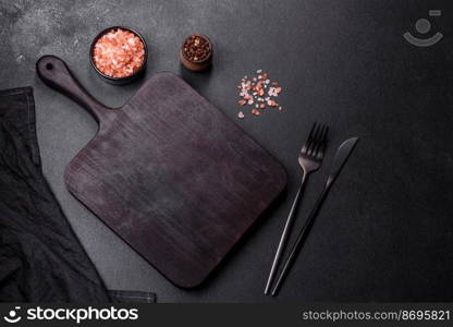 Wooden cutting board with kitchen appliances on a black concrete background. Cooking at home. Wooden cutting board with kitchen appliances on a black concrete background