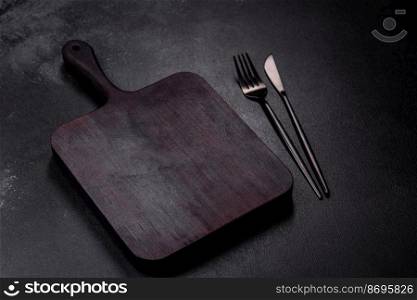 Wooden cutting board with kitchen appliances on a black concrete background. Cooking at home. Wooden cutting board with kitchen appliances on a black concrete background
