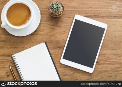 Wooden desk table with tablet, notebook, pencil and cup of coffee. Top view with copy space, flat lay.