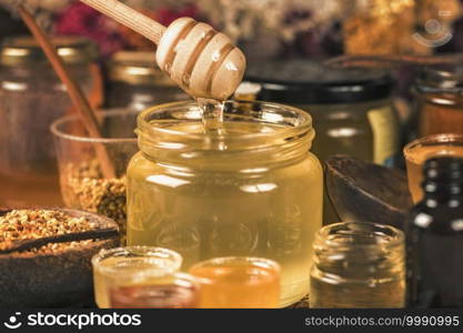 Wooden dipper with honey flowing into glass jar. Various types of honey, honey bee pollen, propolis and wooden honey dipper on table. . Honey Flowing into a Glass Jar