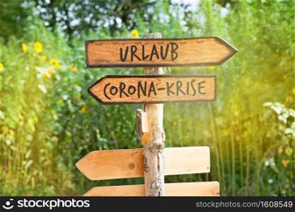 Wooden direction sign with the German words vacation and Corona crisis (Urlaub, Corona-Krise)