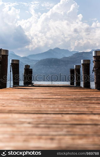 Wooden dock pier, blue lake, mountains and sky with clouds at lago di garda, Italy.