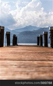 Wooden dock pier, blue lake, mountains and sky with clouds at lago di garda, Italy.