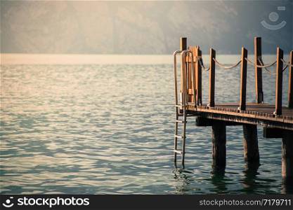 Wooden dock pier extending over blue lake water, mountains at lago di garda