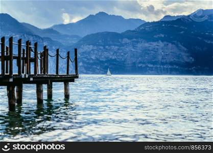 Wooden dock pier extending over blue lake water, mountains at lago di garda
