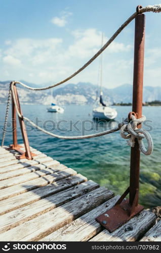 Wooden dock pier in the foreground, sailing boats in the blurry background