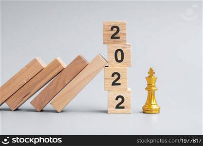 wooden Dominoes falling against 2022 stop blocks with golden Chess King figure. Business, Risk Management, Solution, economic, Insurance and New Year concept