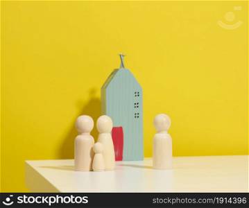 wooden family figurines, model house on a yellow background. Real estate purchase, rental concept. Moving to new apartments