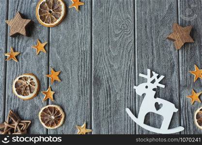 Wooden figure of a white deer on a gray textured wooden background, dried orange slices and stars from the peels of an orange, a tree and wicker.