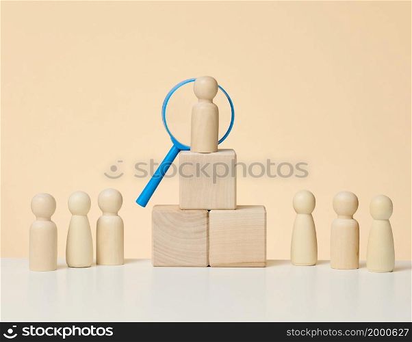 wooden figures of men stand on a beige background and a blue plastic magnifying glass. Recruitment concept, search for talented and capable employees, career growth