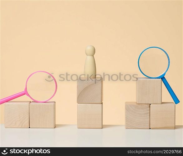 wooden figures of men stand on a beige background and a blue plastic magnifying glass. Recruitment concept, search for talented and capable employees, career growth