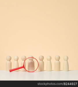 Wooden figures of men stand on a beige background and a blue plastic magnifying glass. Recruitment concept, search for talented and capable employees, career growth