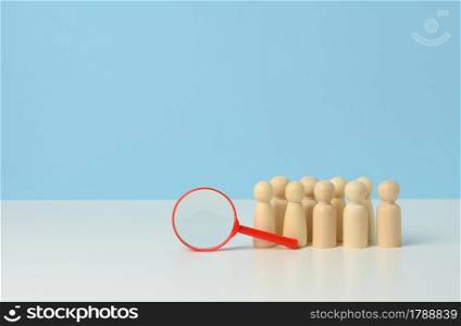 wooden figures of men stand on a blue background and a redplastic magnifying glass. Recruitment concept, search for talented and capable employees, career growth, copy space