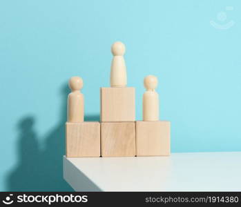 wooden figures of men stand on a pedestal of their cubes on a blue background. The concept of rivalry in sports, business and life. Achieving success and leadership
