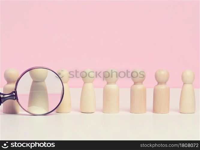 wooden figures of men stand on a pink background and a red plastic magnifying glass. Recruitment concept, search for talented and capable employees, career growth