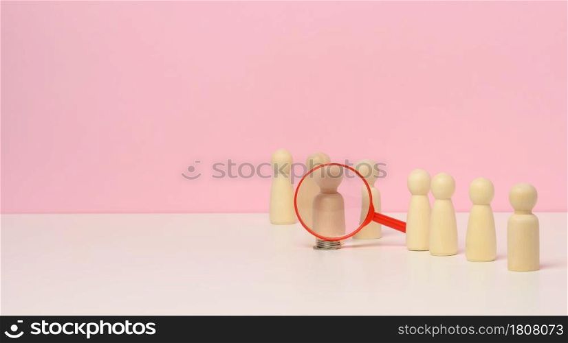 wooden figures of men stand on a pink background and a red plastic magnifying glass. Recruitment concept, search for talented and capable employees, career growth, copy space