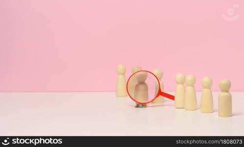 wooden figures of men stand on a pink background and a red plastic magnifying glass. Recruitment concept, search for talented and capable employees, career growth, copy space