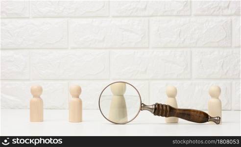 wooden figures of men stand on a white background and a magnifying glass. Recruitment concept, search for talented and capable employees, career growth