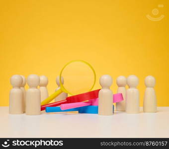 Wooden figures of men stand on a yellow background and a plastic magnifying glass. Recruitment concept, search for talented and capable employees, career growth