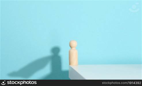 wooden figurine of a man and a shadow with a developing cloak, the concept of the strong and the winner. Everyone is stronger than he thinks, a superhero. Blue background