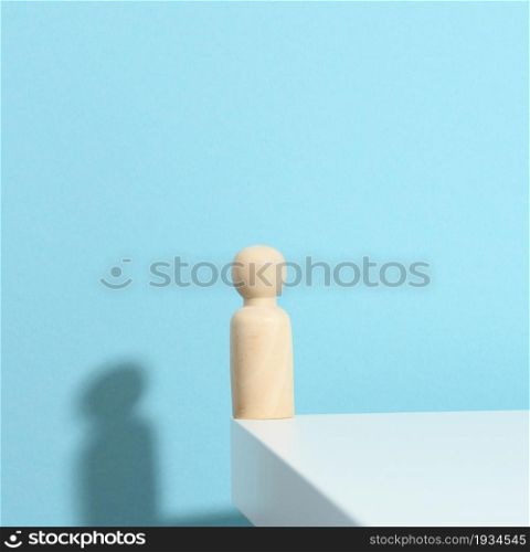 wooden figurine of a man on a blue background with a shadow. The concept of loneliness, sadness and longing