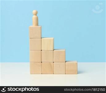 wooden figurine of a man on top of wooden cubes. The concept of purposefulness, achieving goals, overcoming obstacles