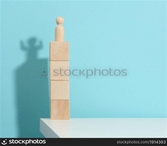 wooden figurine of a man stands high on the cubes, the shadow of a strong and victorious. Everyone is stronger than he thinks, a superhero. Blue background