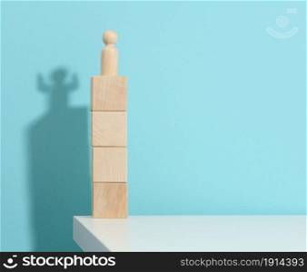 wooden figurine of a man stands high on the cubes, the shadow of a strong and victorious. Everyone is stronger than he thinks, a superhero. Blue background