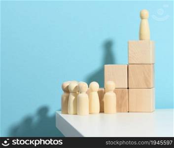 wooden figurine of a man stands on a high podium of cubes, below the crowd. Search for talented employees, rally, manipulation of the masses, selection of employees for the team