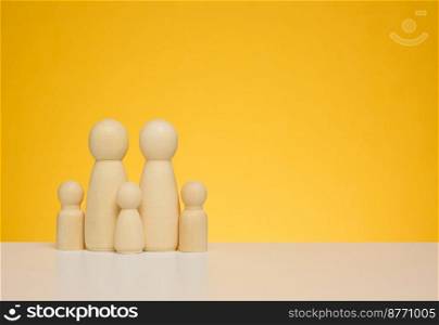 Wooden figurines of a family with children on a yellow background. The concept of protecting low-income families, health insurance