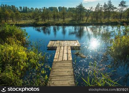 Wooden footbridge on a small lake with a bright sun glare on the water.
