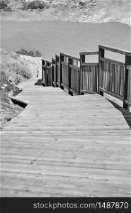 Wooden footpath with railing on the beach. Black and white image
