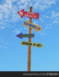 wooden four arrow direction signs post to the nude beach, showers, snacks and a lifeguard against a blue sky