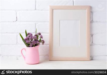 Wooden frame mockup with purple flowers in pink pitcher . Wooden frame mockup with purple field flowers in pink rustic pitcher vase. Empty frame mock up for presentation design. Template framing for modern art.