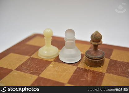 wooden, glass and plastic ponces on the chess board on white background