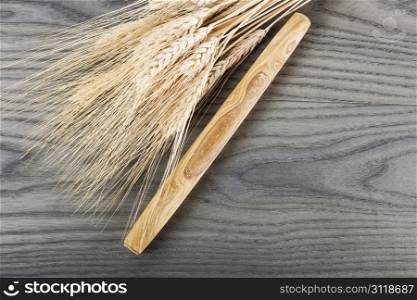 Wooden hand dough roller next to wheat stalk on stressed wood background