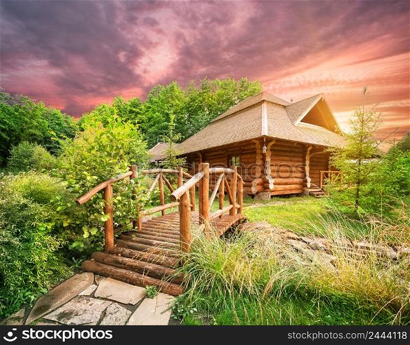 Wooden house and a bridge among greenery under a dramatic evening sky. Wooden house and bridge under dramatic sky