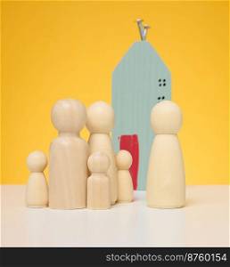 Wooden house and miniature figurines of a family and a realtor on a yellow background. The concept of selling and buying real estate, investment