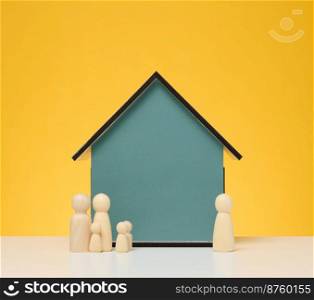 Wooden house and miniature figurines of a family and a realtor on a yellow background. The concept of selling and buying real estate