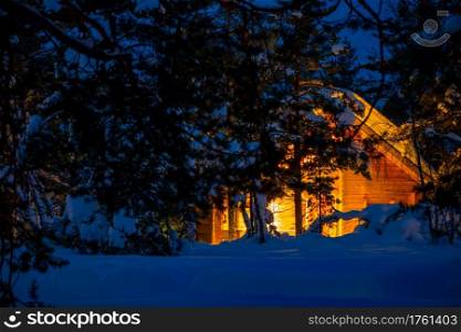Wooden house in the night winter forest. A lot of snow. Illuminated Cottage in a Nightly Snowy Forest